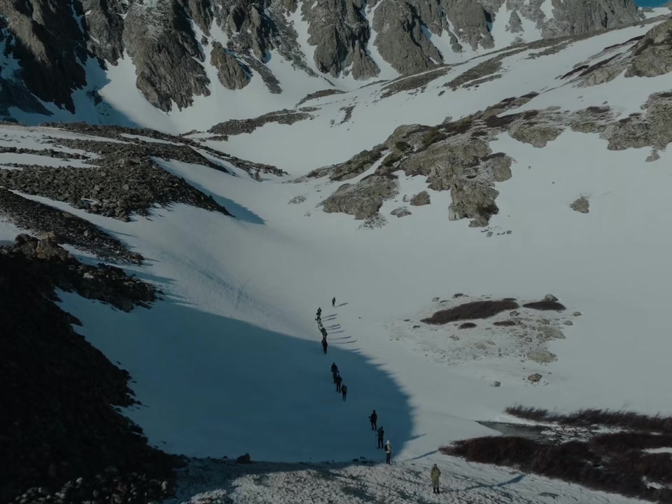 A line of climbers crossing snow above a frozen alpine lake