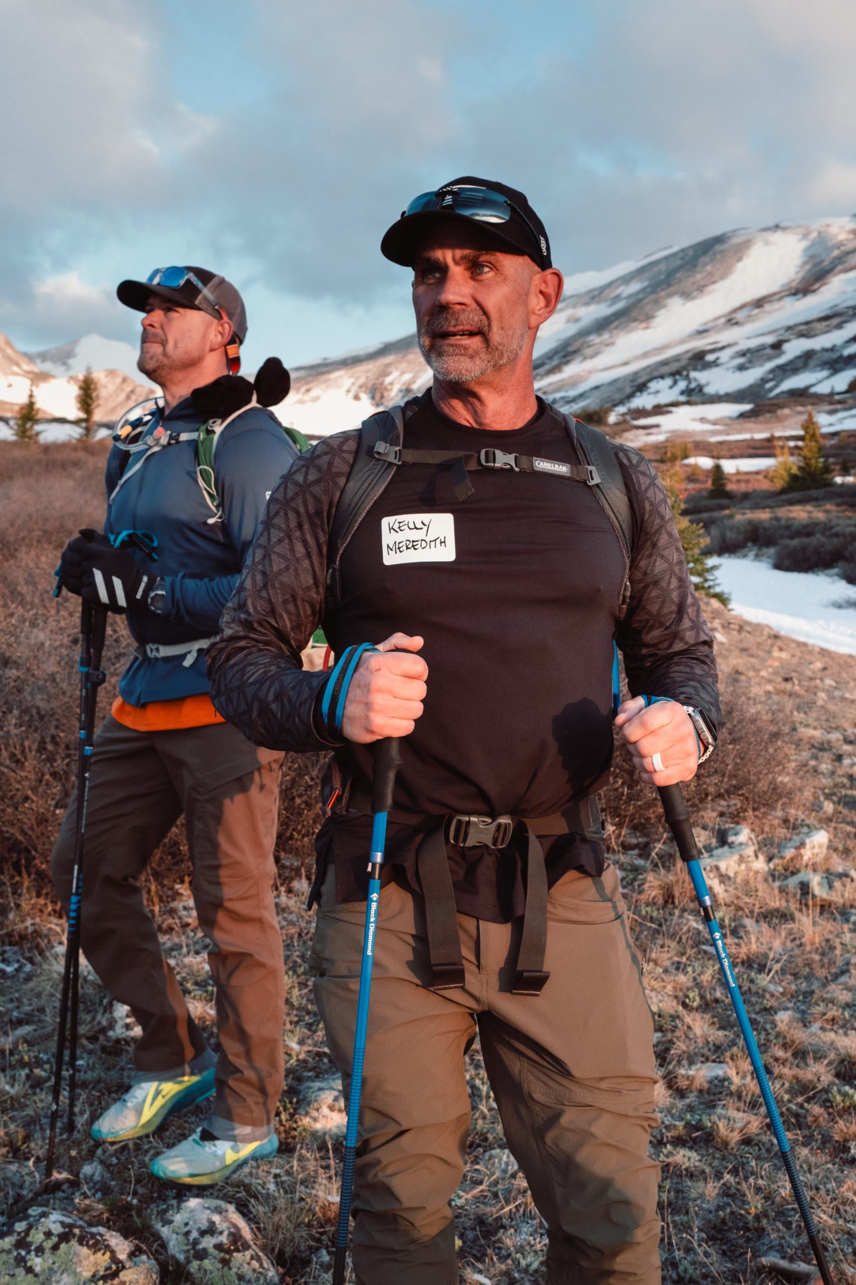 Two athletes with trekking poles looking up the mountain at sunrise