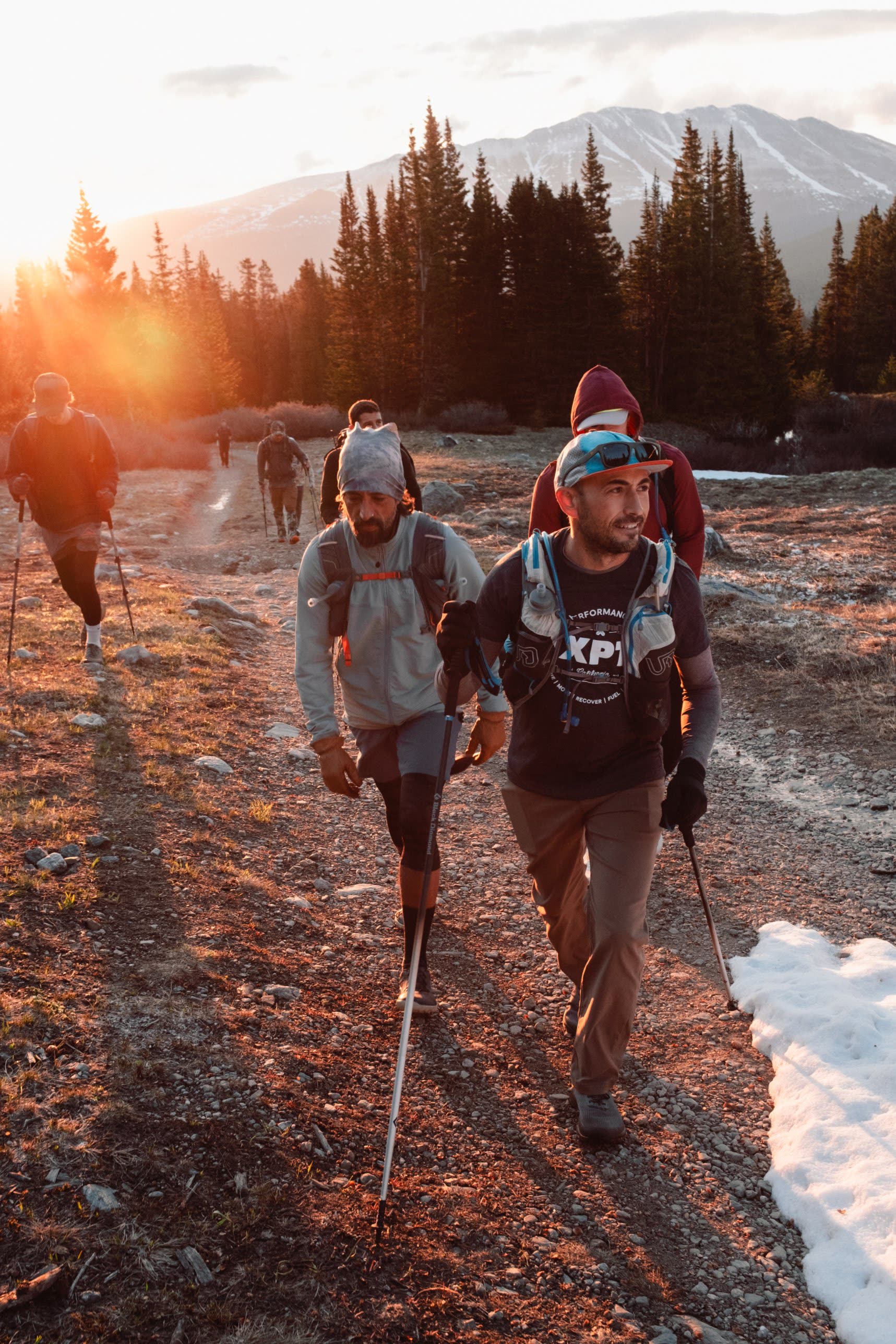 Hikers with poles climbing a trail as the sun rises behind the trees