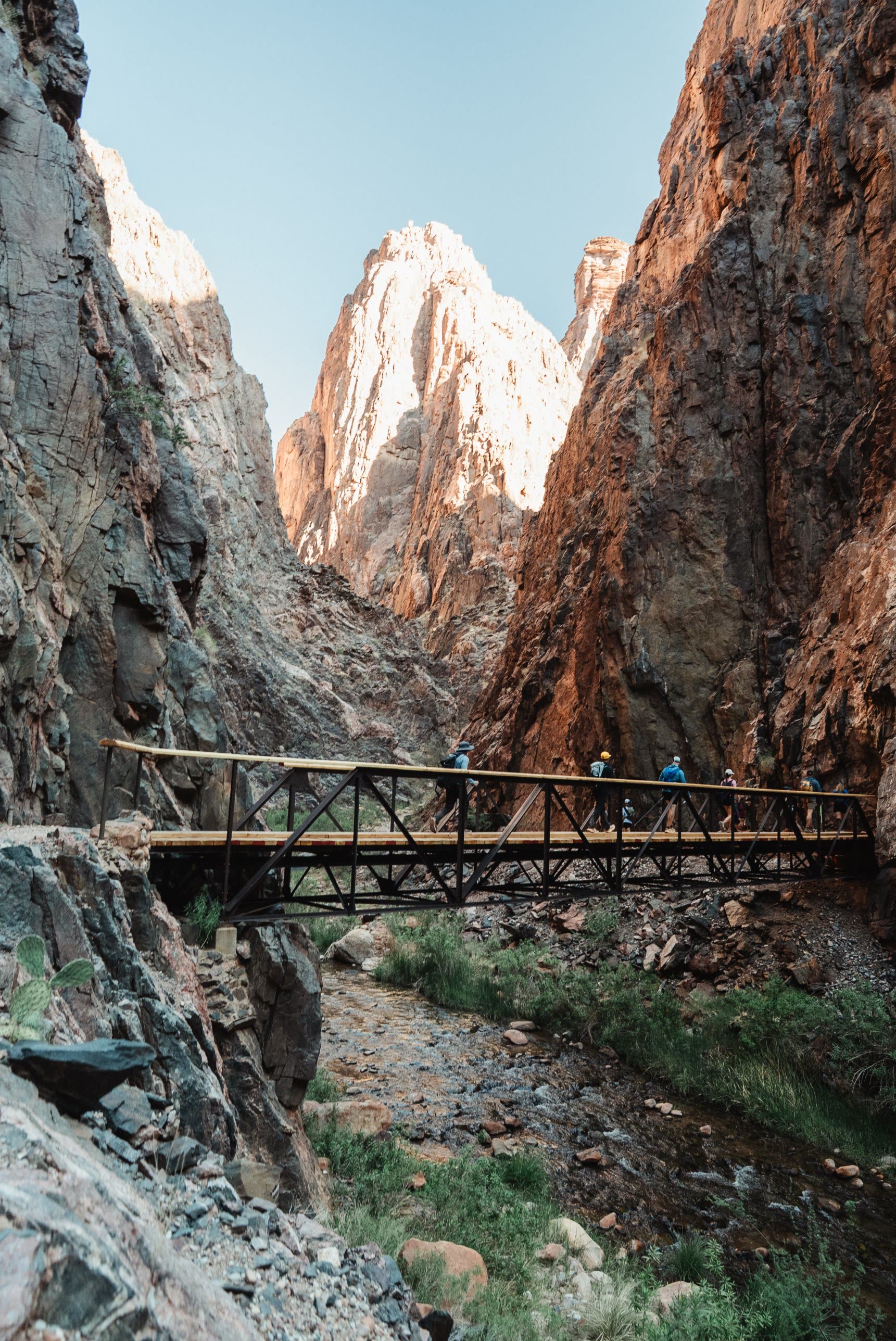 The crew crossing a steel footbridge between towering canyon walls