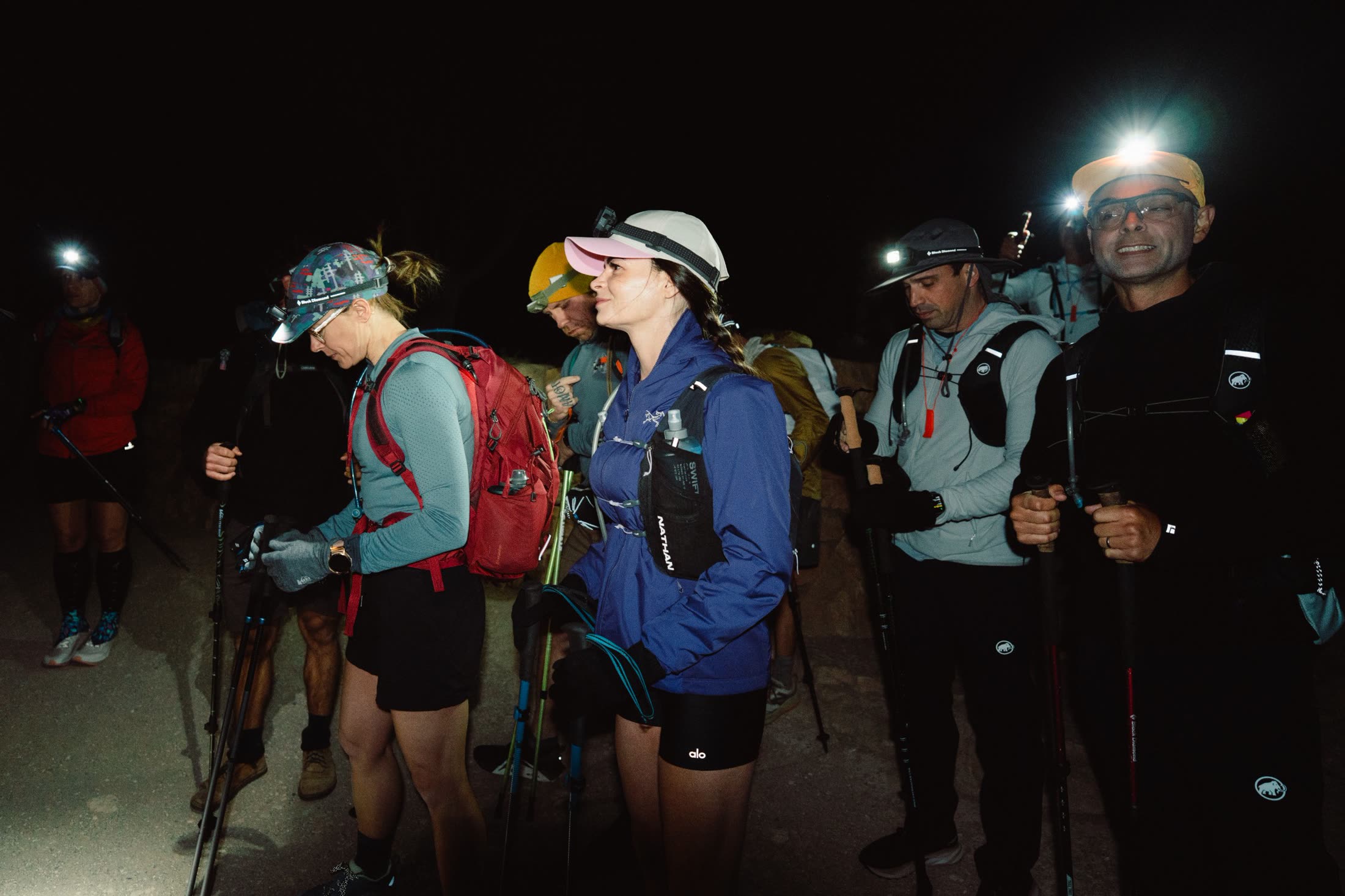 Athletes in headlamps gathering at the trailhead before dawn