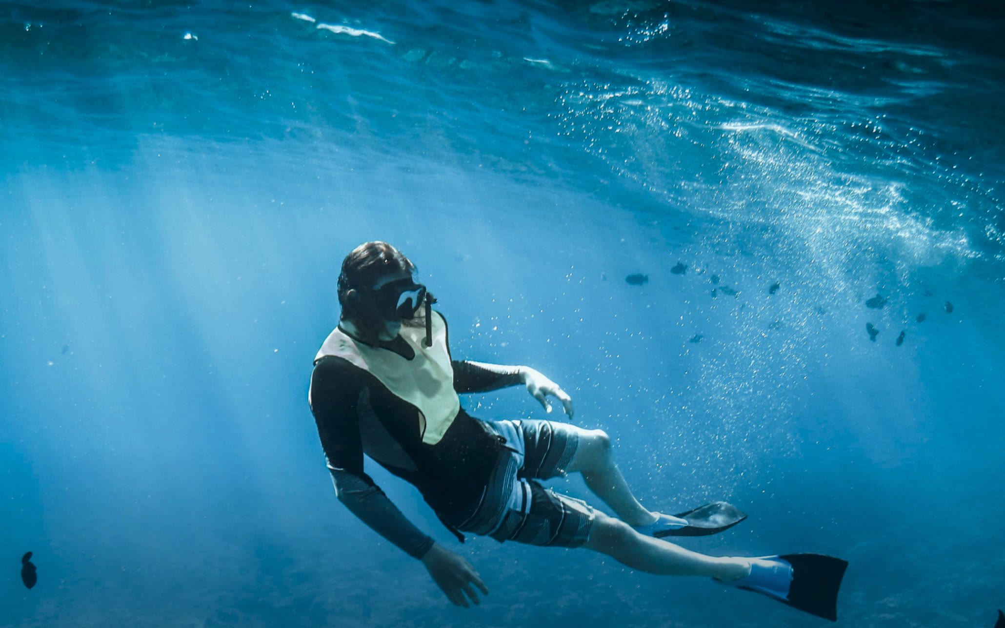 A freediver gliding through sun rays above the reef