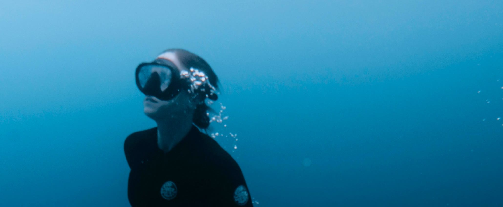 A freediver rising toward the surface trailing bubbles