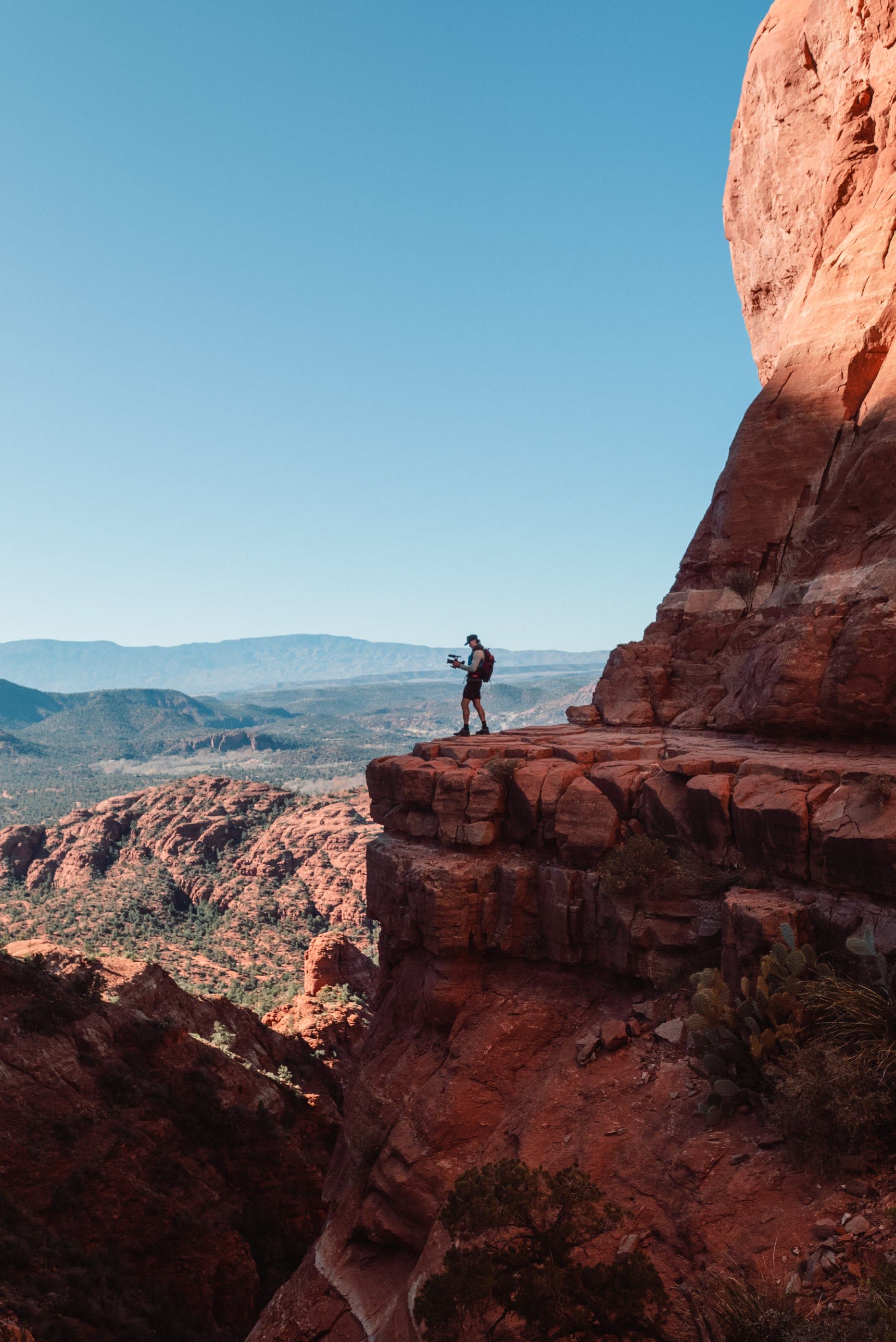 A lone figure on a red rock ledge above a wide desert valley