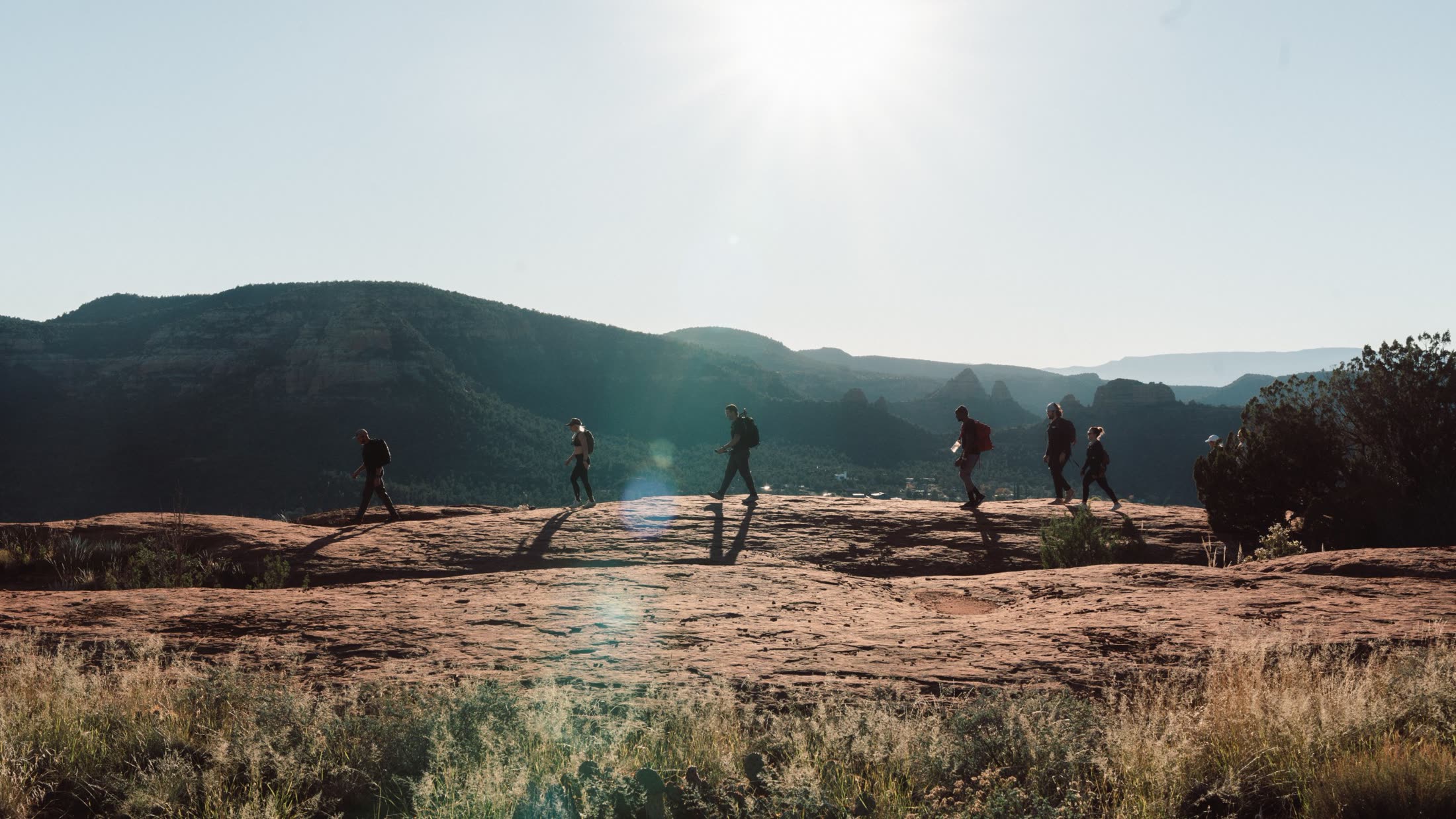 A line of ruckers silhouetted crossing slickrock with mesas behind