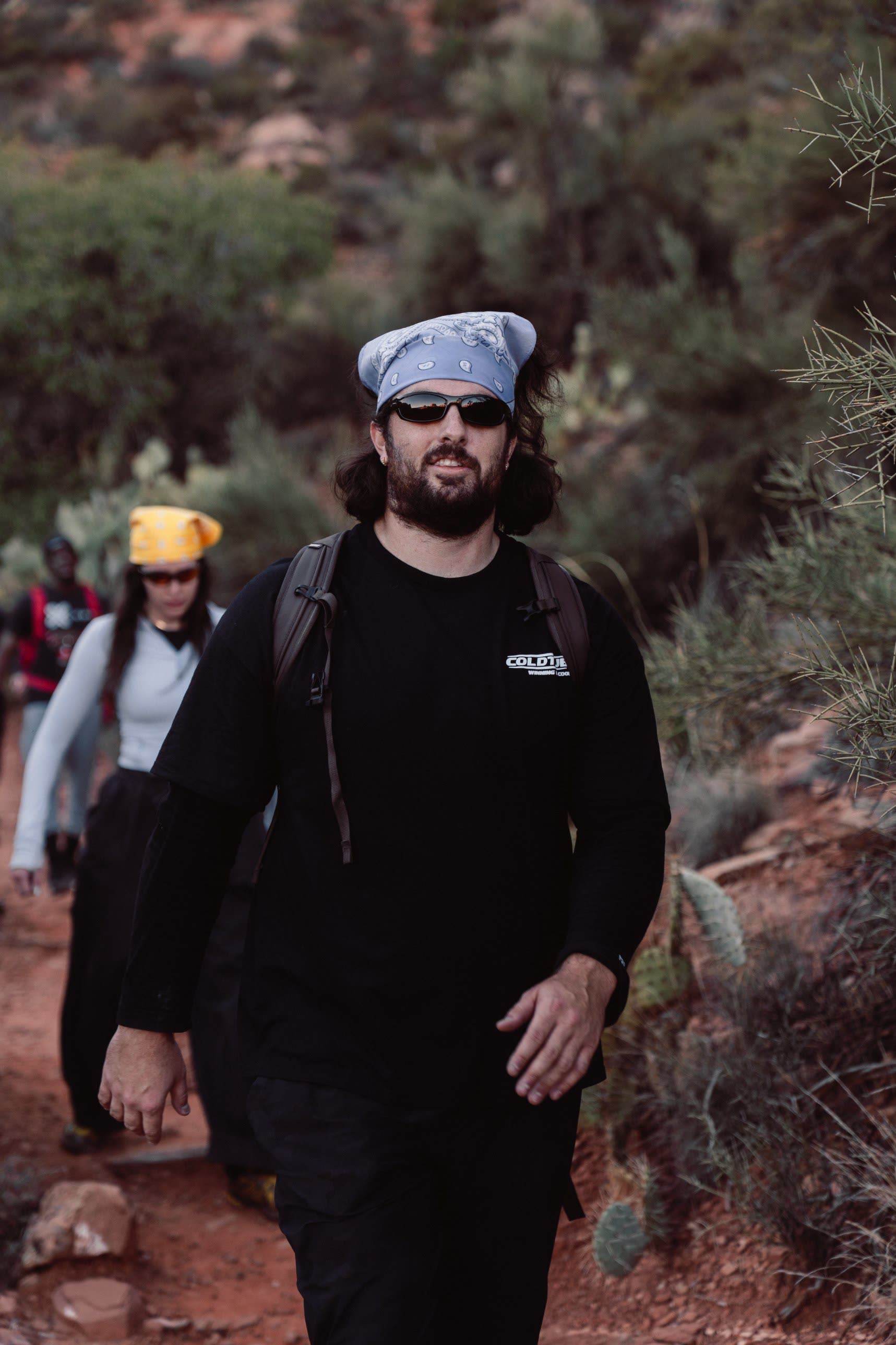 Athletes in bandanas walking a red dirt trail through cactus and scrub