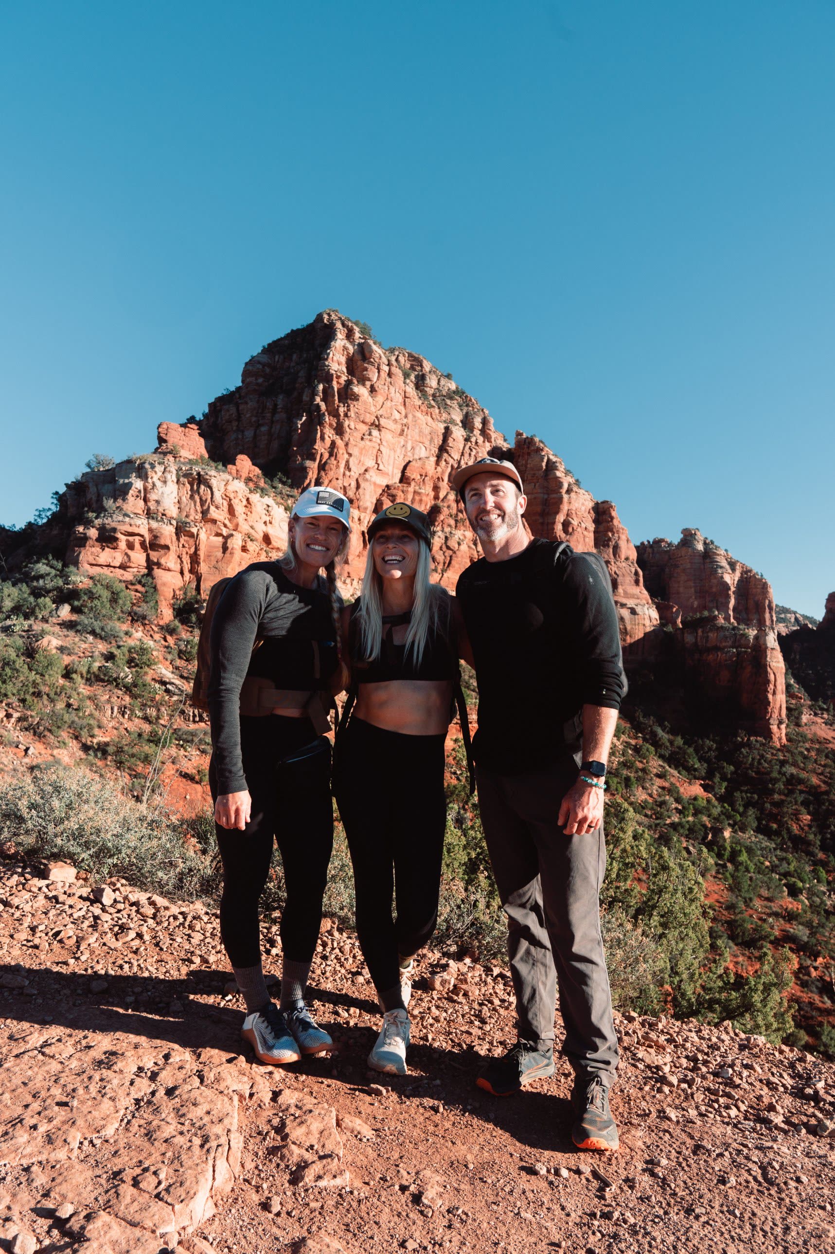 Three athletes smiling together in front of a red rock peak